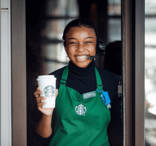 A smiling barista holding a customer's drink.