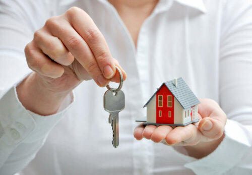 An agent gifting the keys to a house and holding a small plastic house.