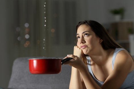 A person holding a pan under the ceiling to collect water from torrential rain
