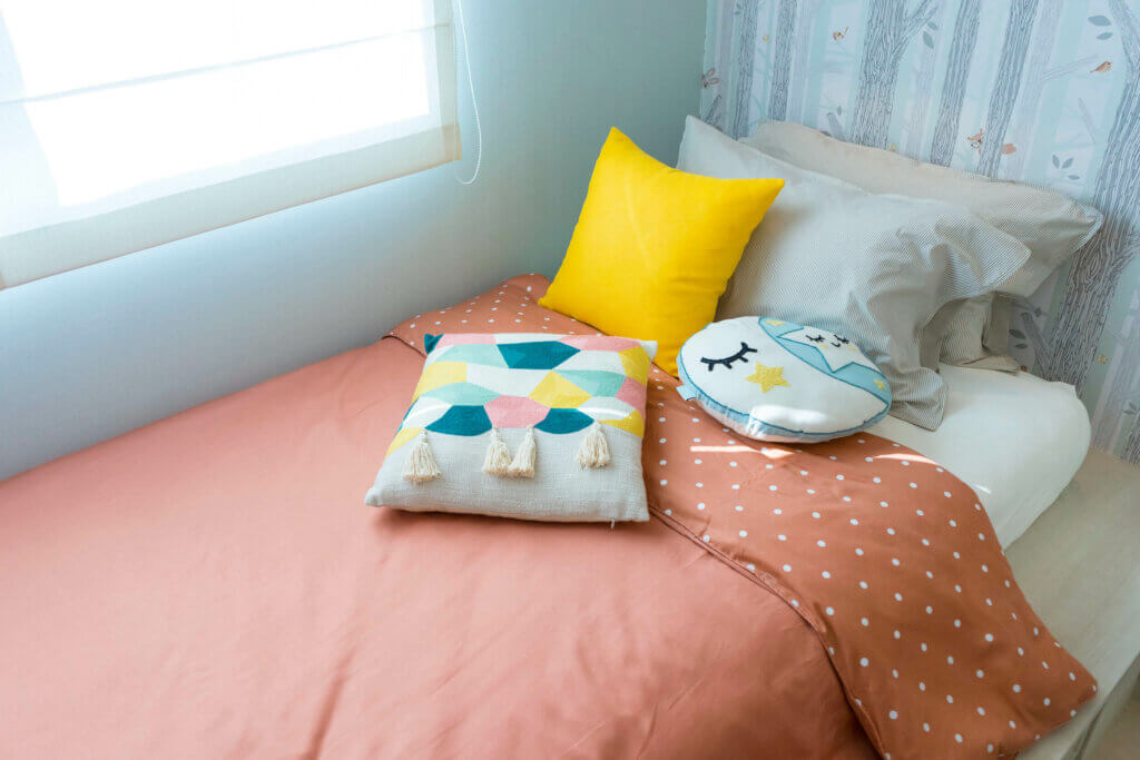 A child's bed with pink and yellow bedclothes.