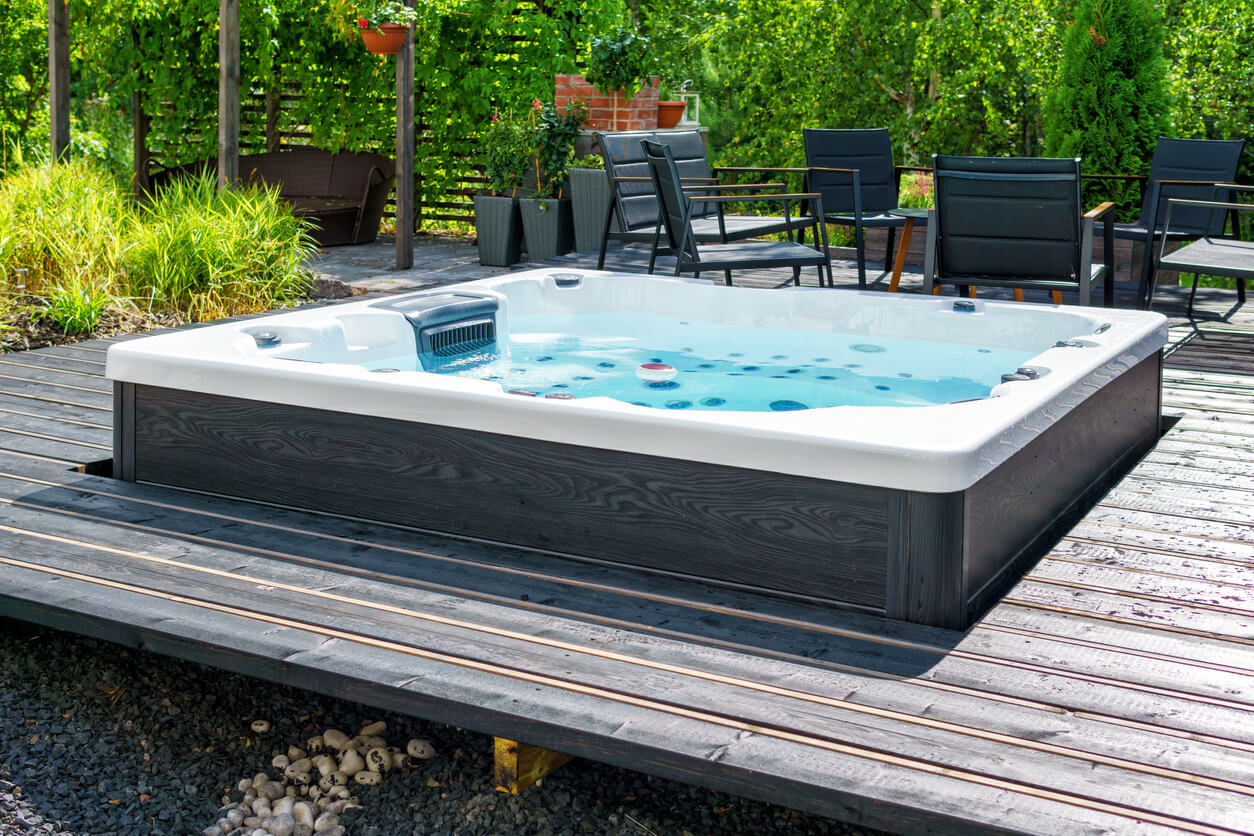 Large hot tub embedded in the backyard terrace. A sunny summer's day in the shelter of a green garden. Everyday luxury and relaxation in your own backyard. Spa complex, vacation and traveling concept.