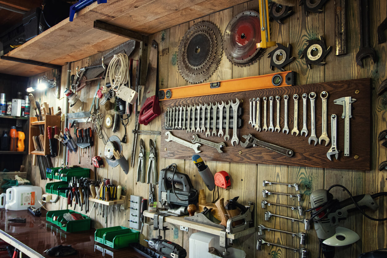 Various repair tools hang on a wooden wall in a workshop