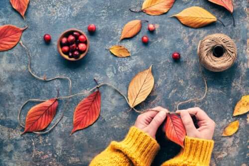 A person putting together a fall garland using dried fall leaves and red cranberries.