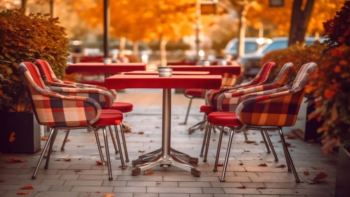Plaid upholstered chairs around red tables in a restaurant's outdoor dining area on a sunny fall day.