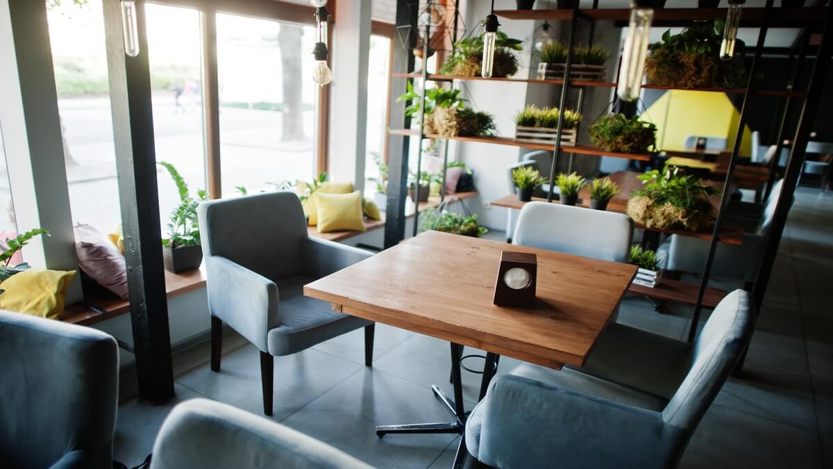 Cushioned gray arm chairs around wooden tables in an industrial style restaurant.